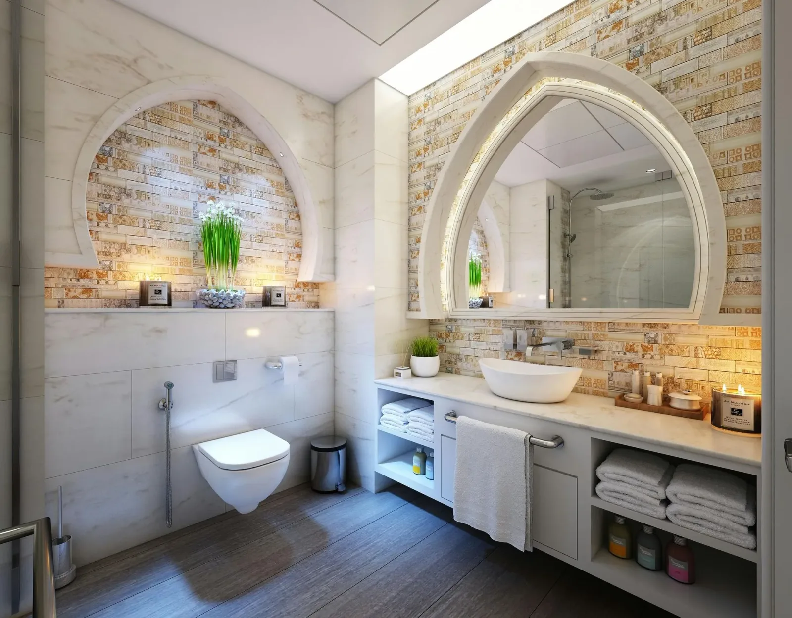 Wide view of a marble bathroom with an arched mirror and gold mosaic tiling