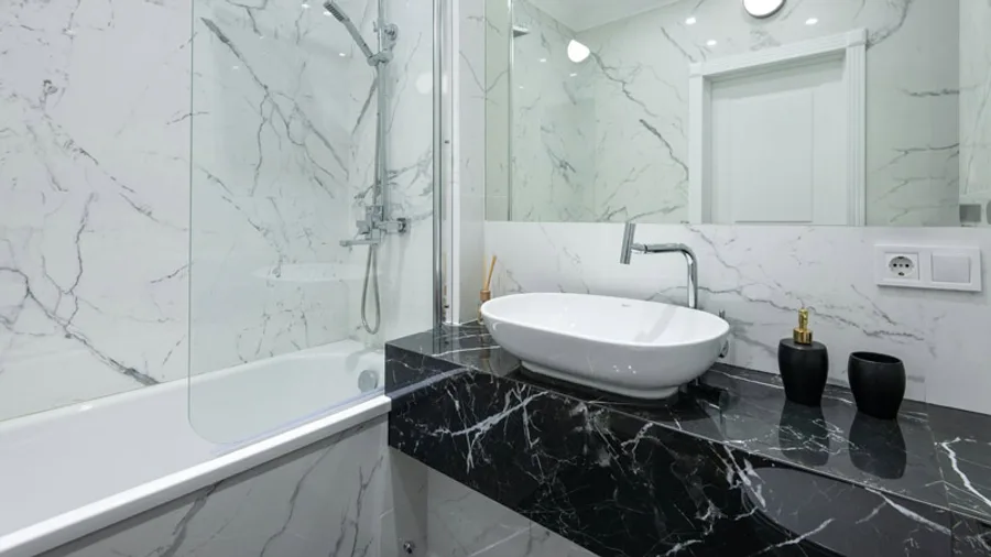 Bathroom with a vessel sink on a black marble vanity and a glass tub screen